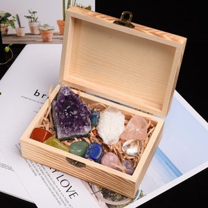 May include: A wooden box with a hinged lid, filled with various colorful crystals and stones. The crystals include amethyst, quartz, and other polished stones in shades of purple, white, pink, and green. The box is lined with straw.