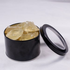 May include: A black round tin with a clear lid filled with translucent yellow rock candy.