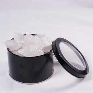 May include: A black metal tin with a clear lid filled with white crystal rocks.