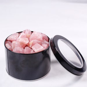 May include: A black metal tin with a clear lid filled with pink rose quartz crystals.