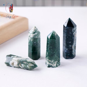 Puede incluir: Cuatro puntas de cristal de ágata verde y blanca, también conocidas como ágata musgo, sobre una superficie blanca. Los cristales están pulidos y tienen un acabado liso y brillante.