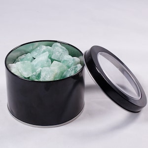 May include: A black metal tin with a clear lid filled with green fluorite crystals.
