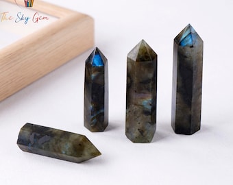 May include: Four labradorite crystal points of varying sizes, with iridescent blue and green hues, on a white surface.
