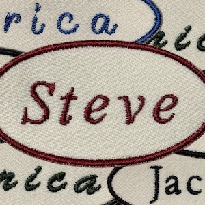 May include: A white oval-shaped fabric patch with a maroon border. The name "Steve" is embroidered in maroon thread.