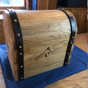 Puede incluir: Un cofre del tesoro de madera con una cerradura y una llave de latón. El cofre está decorado con correas de cuero negro y tachuelas de latón.