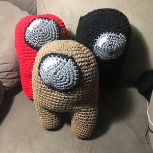 May include: Three crocheted plush toys shaped like the characters from the video game Among Us. The toys are red, brown, and black.
