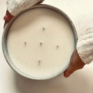 May include: A large, round, grey concrete candle vessel filled with smooth, off-white wax. The candle features five distinct wicks arranged in a cross pattern across the surface. The container has a thick, textured rim and a flat, circular base.