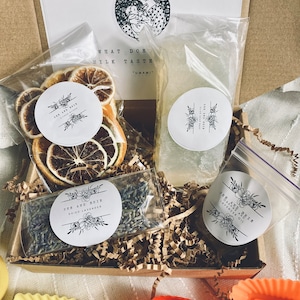 May include: A brown cardboard box filled with brown packing paper. The box contains a variety of items, including dried citrus fruit, lavender, and a clear bottle of liquid. The box also includes a white card with the text "What does milk taste like? "Umami" ".