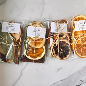 May include: Four clear plastic bags containing dried potpourri mixes, each labeled She & Brie. The contents include dried orange slices, cinnamon sticks, bay leaves, star anise, and other botanicals, tied with natural raffia twine strings.