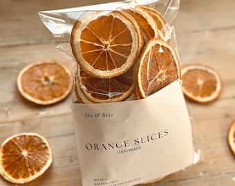 May include: A clear plastic bag filled with dried orange slices. The bag has a white label with the text "She & Brie ORANGE SLICES HANDMADE SET OF 21 NATURAL FRUIT HANDMADE IN SAN FRANCISCO".