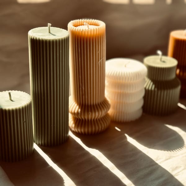 Puede incluir: Una colección de seis velas de pilar de diversas formas y tamaños, con texturas acanaladas verticales. Las velas son de tonos verde salvia, beige, blanco y marrón, cada una rematada con una mecha de algodón centrada para encenderlas.