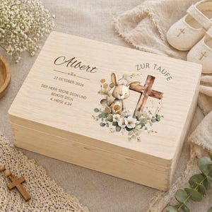 Op de afbeelding: Een licht houten kistje met de naam "Albert" en de datum "22 OKTOBER 2026" op het deksel. De kist is versierd met een aquarel illustratie van een konijn, kruis en bloemen. Een brandende kaars en babyschoentjes zijn in de buurt.