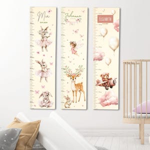 Op de afbeelding: Drie decoratieve groeimeters met grillige illustraties. De meters tonen konijnen, een fee, een hert en een teddybeer in een vliegtuig. Elke meter heeft een naam en een datum, met metingen in centimeters. Het kleurenpalet omvat zachtroze, beige en wit.