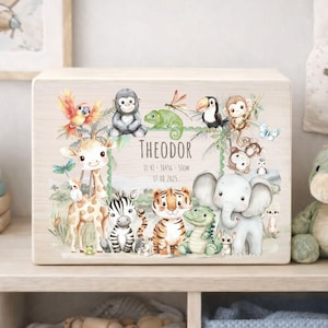 Könnte beinhalten: Eine Holzkiste mit einer Dschungel-Illustration, die verschiedene Tiere zeigt, darunter eine Giraffe, ein Zebra, ein Tiger und ein Elefant. Der Name "Theodor" ist zusammen mit Maßen und einem Datum abgebildet. Die Kunstwerke sind in sanften Pastellfarben gehalten.