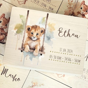 Op de afbeelding: Houten plaat met een illustratie van een leeuwenwelp op een schommel. De naam "Ethan", datum, tijd, gewicht en lengte zijn vermeld. Andere platen met eekhoorn- en leeuwenwelp-illustraties zijn zichtbaar.