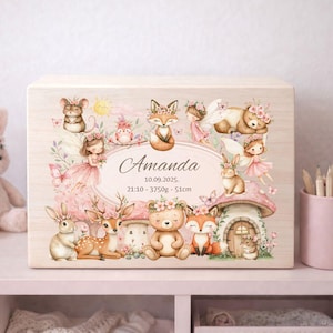May include: Wooden keepsake box decorated with a forest scene, including animals and fairies. The box is personalised with the name "Amanda" and birth details. The design features soft pink and beige colours, creating a gentle aesthetic.
