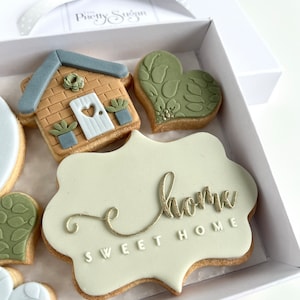 Op de afbeelding: Een set gedecoreerde koekjes in een witte doos. De koekjes zijn versierd met een huis, harten en de woorden "Sweet Home".