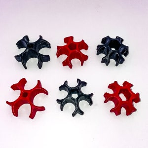 Può includere: Sei oggetti a forma di stella stampati in 3D. Tre sono neri e tre sono rossi. Gli oggetti hanno una forma a stella a cinque punte con un foro al centro di ogni punta.