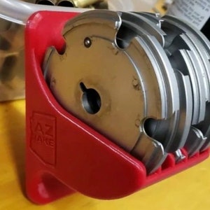 May include: A red plastic holder with the text "AZ TAKE" on it holds a stack of five silver reloading dies.