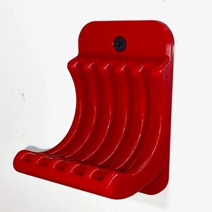 May include: Red plastic wall mount with five curved hooks for hanging items. The mount has a single screw hole at the top.