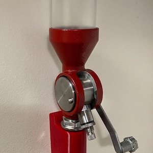 May include: A red metal wall-mounted beer dispenser with a clear plastic tube and a silver handle. The dispenser has a red plastic base.