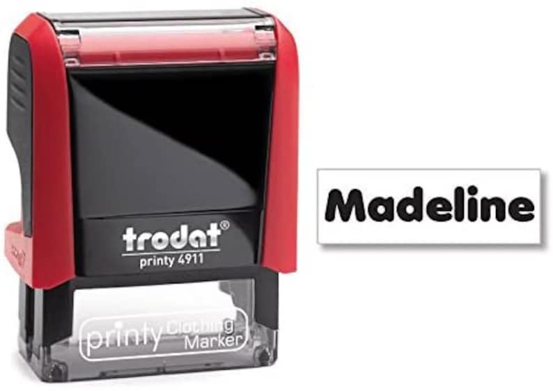 May include: Red and black self-inking stamp with the text "trodat printy 4911" and "printy clothing marker" on the front. The stamp is labeled with the name "Madeline" in black text on a white background.