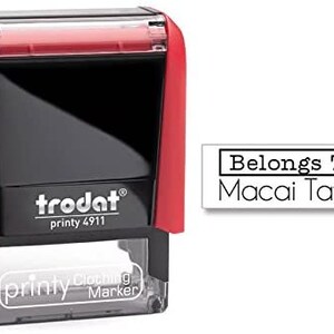 May include: Red and black self-inking stamp with a clear top. The stamp reads "trodat printy 4911" and "printy Clothing Marker". The stamp is designed to print "Belongs To: Macai Taylor".