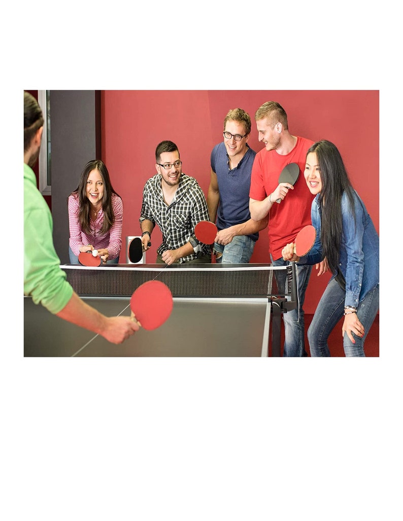 May include: A group of people playing table tennis. They are using red and black paddles and a white ball. The table is black and has a net in the middle. The people are smiling and having fun.