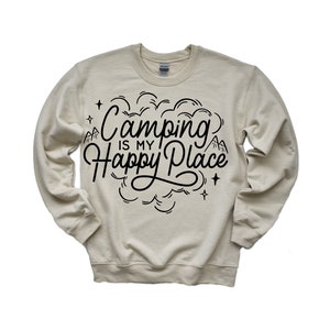 Może przedstawiać: Beżowa bluza z czarnym napisem "Camping is my Happy Place" z grafiką g&oacute;ry i gwiazdy.
