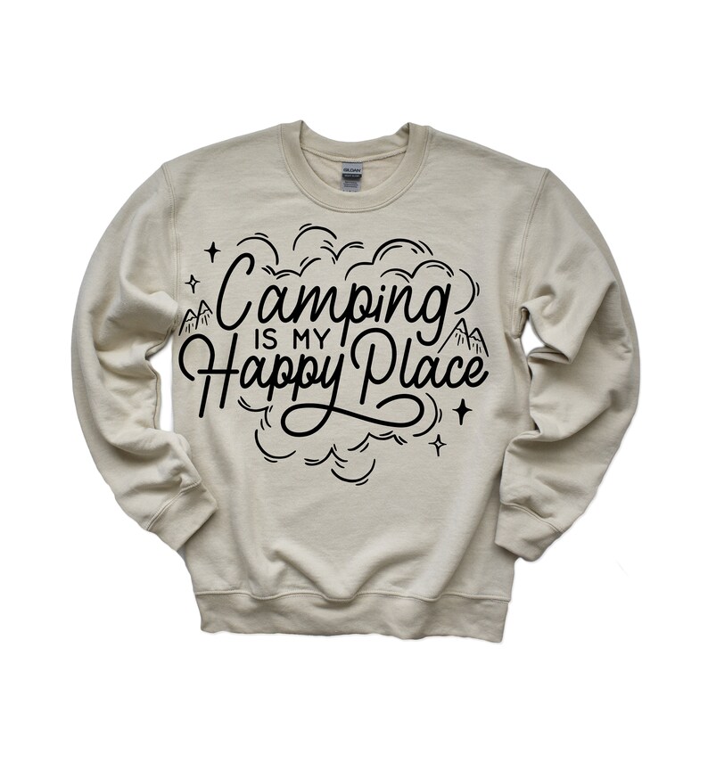 Może przedstawiać: Beżowa bluza z czarnym napisem "Camping is my Happy Place" z grafiką g&oacute;ry i gwiazdy.