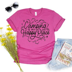 Może przedstawiać: R&oacute;żowa koszulka z czarnym napisem "Camping is my happy place" z grafiką g&oacute;ry i gwiazdy.
