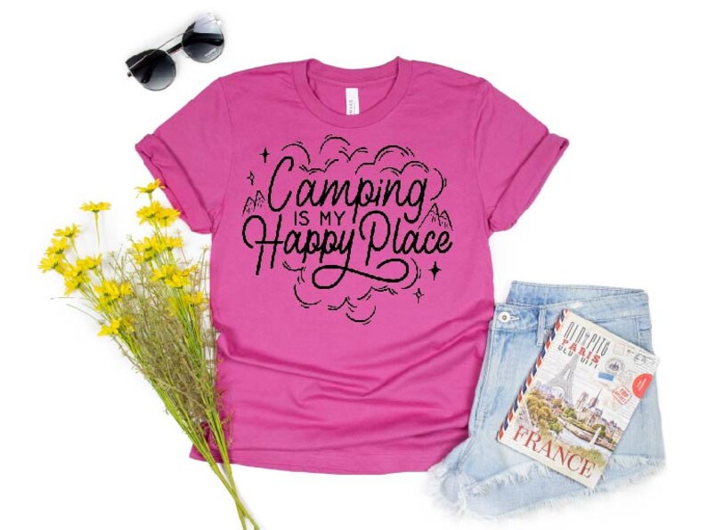 Może przedstawiać: R&oacute;żowa koszulka z czarnym napisem "Camping is my happy place" z grafiką g&oacute;ry i gwiazdy.