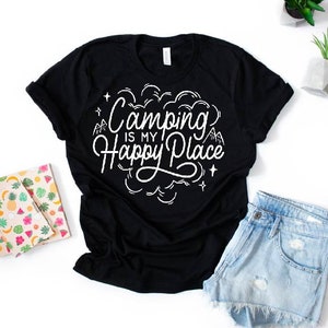 Może przedstawiać: Czarny T-shirt z białym napisem "Camping is my Happy Place". Tekst jest w stylizowanym foncie i zawiera małe rysunki g&oacute;r i gwiazd.