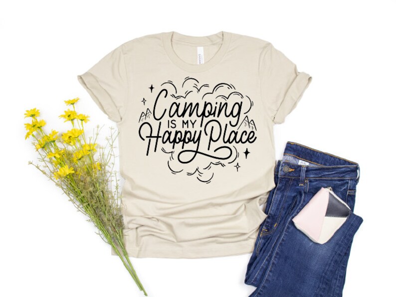 Może przedstawiać: Beżowa koszulka z czarnym nadrukiem, na kt&oacute;rym widnieje napis "Camping is my Happy Place" z wzorem g&oacute;r i chmur.