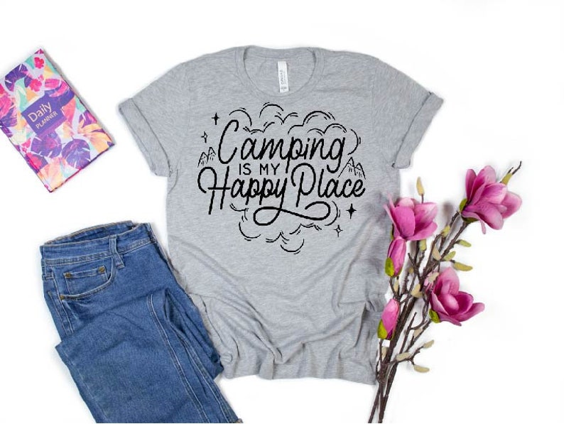 Może przedstawiać: Szary T-shirt z napisem "Camping is my Happy Place" w czarnym kolorze. Tekst jest otoczony wzorem chmury z gwiazdami i g&oacute;rami.