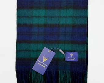 May include: A rectangular scarf featuring a dark green and navy blue plaid pattern with a soft, fuzzy texture and fringed ends. A purple tag attached by a string displays the text House of Heritage PURE LAMBSWOOL with a gold deer logo.