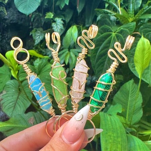 Puede incluir: Cuatro anillos de alambre dorado envueltos con piedras de cristal de diferentes colores. Los anillos presentan una piedra verde, azul, rosa y verde.