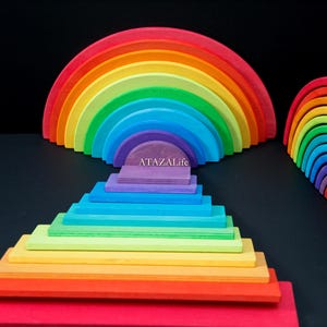May include: A set of wooden rainbow stacking arches and rectangular building blocks in a spectrum of colors including red, orange, yellow, green, blue, and purple. The text ATAZALife is printed on the smallest purple arch and block.