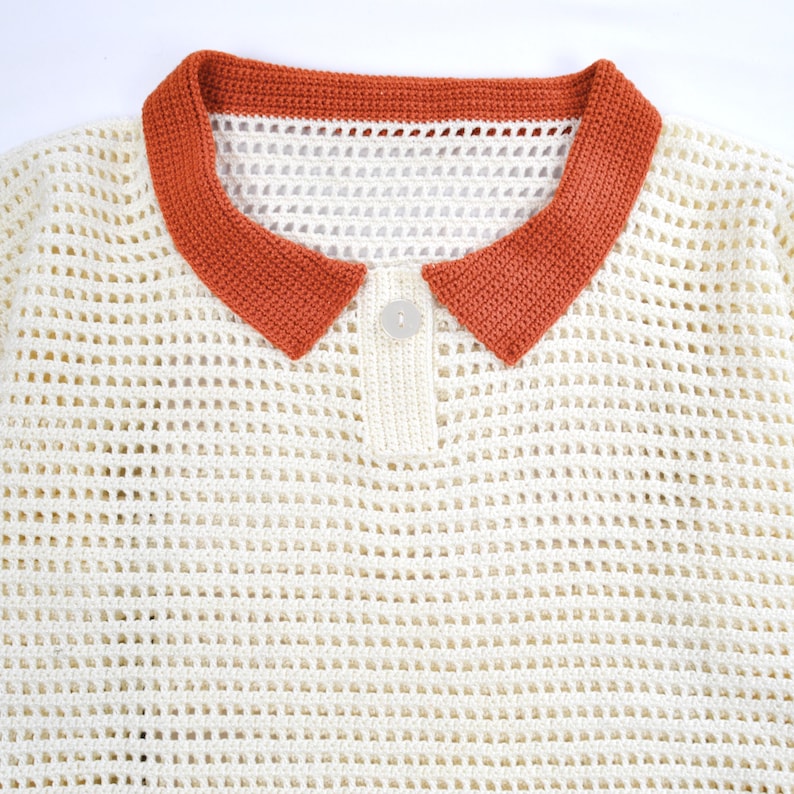 Pode incluir: Camisa polo creme com tecido aberto e gola cor de ferrugem. A camisa apresenta uma carcela com bot&otilde;es e um &uacute;nico bot&atilde;o redondo branco sujo. A gola &eacute; de cor lisa, enquanto o corpo tem um design de malha aberta texturizada.