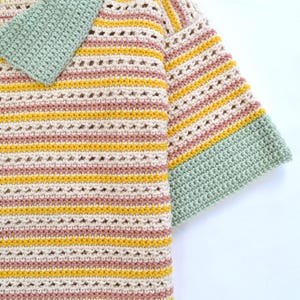 Puede incluir: Un top de crochet a rayas con cuello y pu&ntilde;os verdes. El top est&aacute; hecho con hilo beige claro y tiene rayas rosas y amarillas.