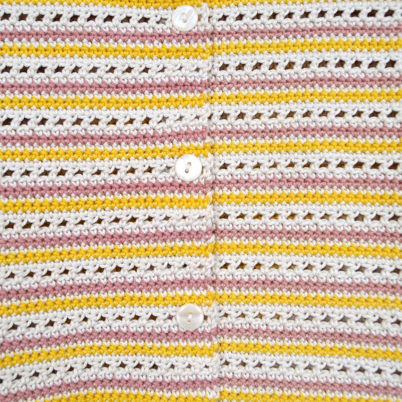 Puede incluir: Primer plano de un c&aacute;rdigan de crochet blanco con rayas rosas y amarillas. El c&aacute;rdigan tiene cierre de botones.