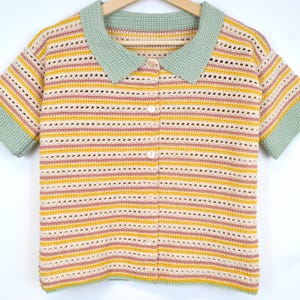 Puede incluir: Un top de crochet a rayas con cuello y mangas cortas. El top est&aacute; hecho en una combinaci&oacute;n de colores amarillo claro, rosa y verde.