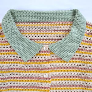 Puede incluir: Un su&eacute;ter de crochet a rayas con un cuello verde y botones blancos. El su&eacute;ter tiene un patr&oacute;n de rayas rosa claro, crema y amarillo.