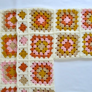 May include: A crocheted blanket with a geometric pattern in shades of pink, orange, brown, and white.
