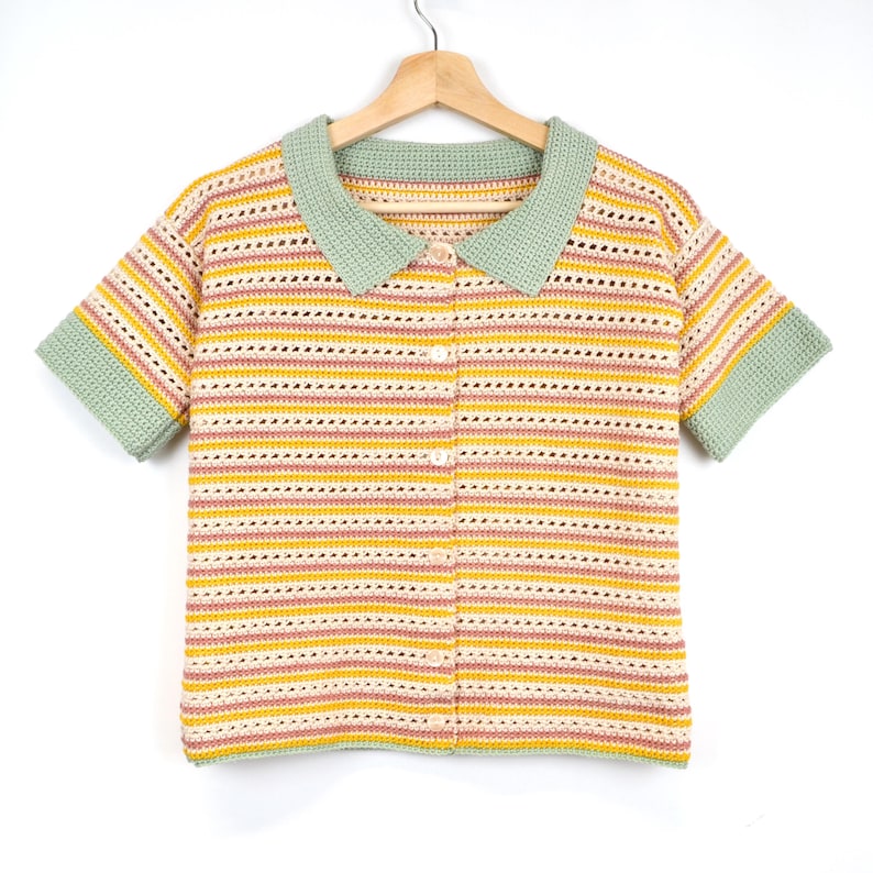 Puede incluir: Un top de crochet a rayas con cuello y mangas cortas. El top es en tonos de amarillo, rosa y blanco, con un ribete verde alrededor del cuello y las mangas.