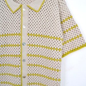 Puede incluir: Una camisa de crochet beige con mangas cortas y cuello. La camisa presenta rayas horizontales amarillas y se abrocha en la parte delantera con botones nacarados. Los bordes del cuello y las mangas est&aacute;n ribeteados en amarillo.