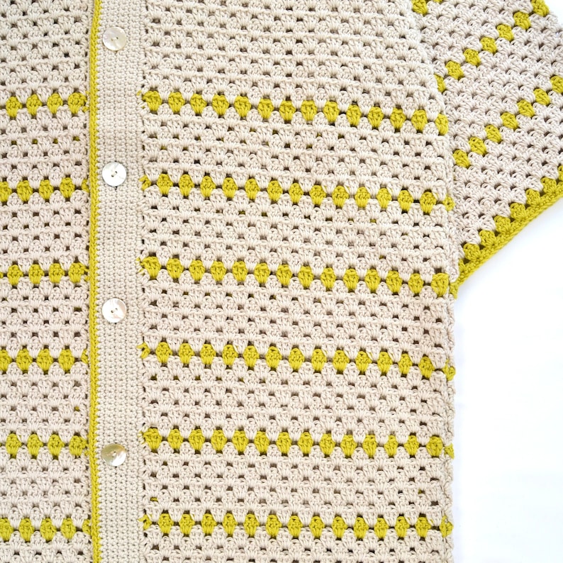 Puede incluir: Camisa de crochet color crema con botones y mangas cortas. La camisa presenta un patr&oacute;n repetitivo de formas de diamante amarillas. Los bordes y la tapeta de botones son de color crema a juego.