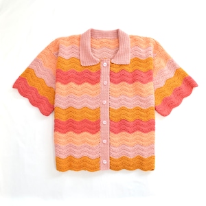 May include: A crocheted button-up shirt with a wavy striped pattern in shades of pink, orange, and yellow. The shirt has short sleeves and a collared neckline.