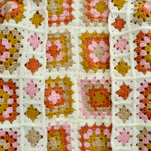 May include: A crocheted blanket with a granny square pattern in shades of pink, orange, brown, and yellow.