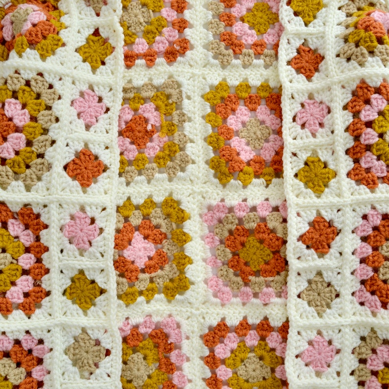 May include: A crocheted blanket with a granny square pattern in shades of pink, orange, brown, and yellow.